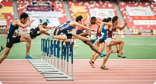Atleta de salto com vara ultrapassando a barra nas séries finais de um campeonato de atletismo em pista coberta numa arena moderna